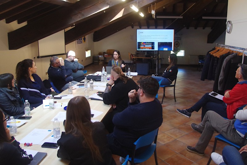 People around a meeting table listening to a presentation about a digital practice in first aid training.